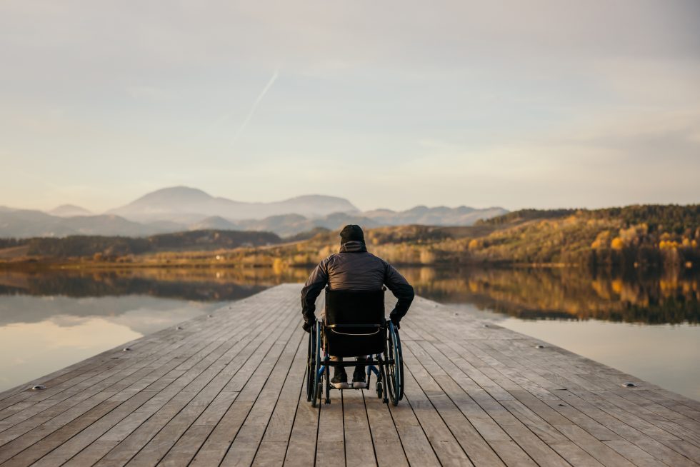 Man in wheelchair on pier overlooking serene lake